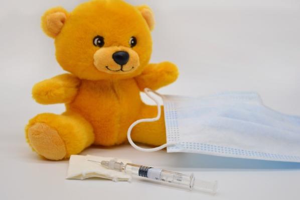 Teddy bear sitting next to face mask and needle